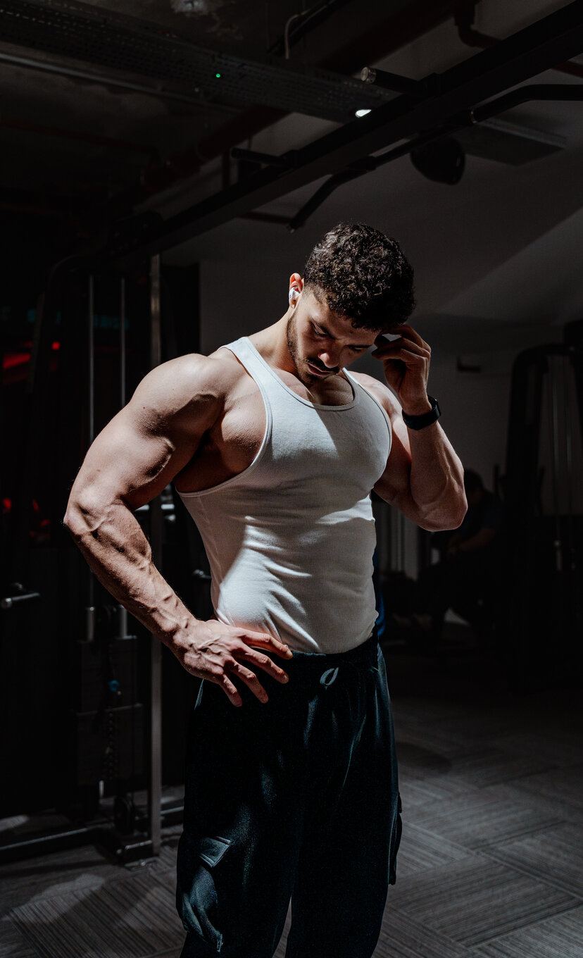 Bogdan Calinescu in a white tank top, standing, hand at his hairline, looking down
